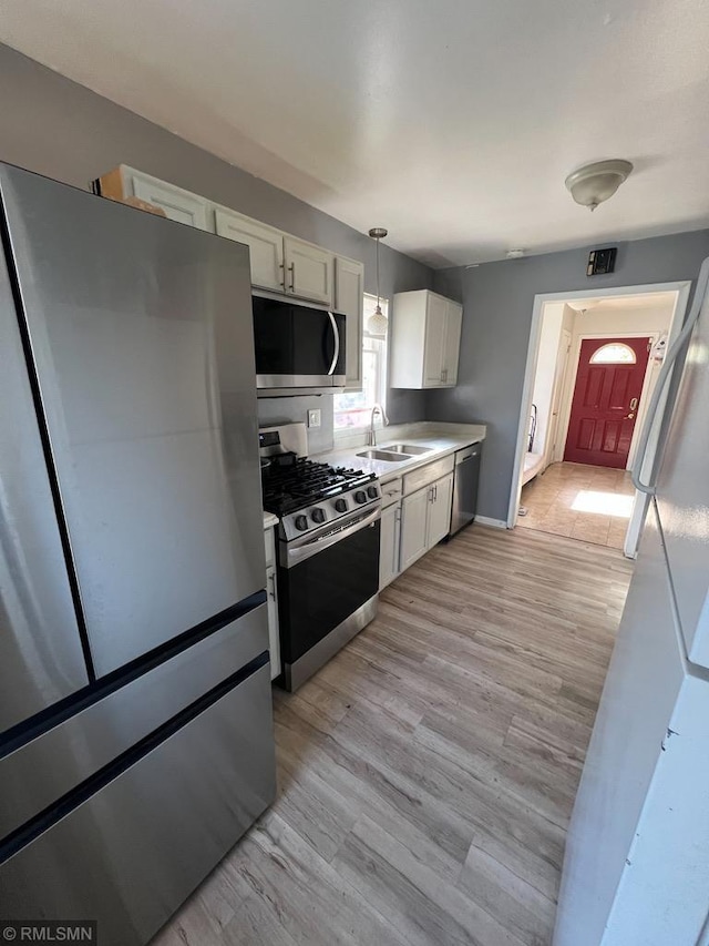 kitchen with pendant lighting, light wood-type flooring, stainless steel appliances, and white cabinets