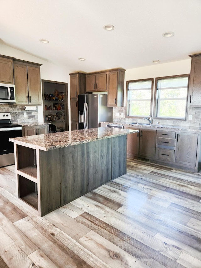 kitchen featuring appliances with stainless steel finishes, light stone counters, a kitchen island, light wood-type flooring, and decorative backsplash