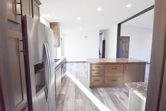 kitchen featuring a center island, vaulted ceiling, light hardwood / wood-style flooring, light stone countertops, and appliances with stainless steel finishes