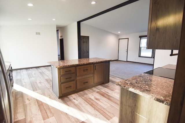 kitchen featuring dark stone countertops, light hardwood / wood-style flooring, vaulted ceiling, and a center island