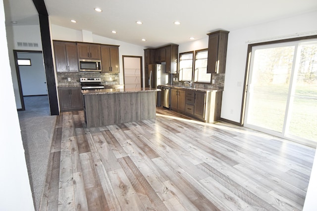 kitchen featuring a kitchen island, light wood-type flooring, appliances with stainless steel finishes, decorative backsplash, and vaulted ceiling