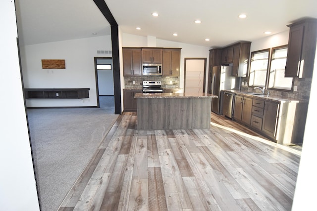 kitchen with lofted ceiling, a center island, tasteful backsplash, light wood-type flooring, and appliances with stainless steel finishes