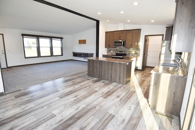 kitchen featuring stainless steel appliances, light stone countertops, sink, vaulted ceiling, and light colored carpet