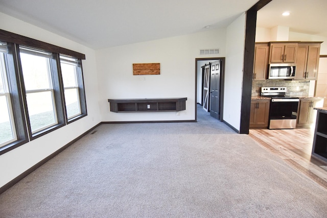 unfurnished living room with light carpet, a healthy amount of sunlight, and vaulted ceiling