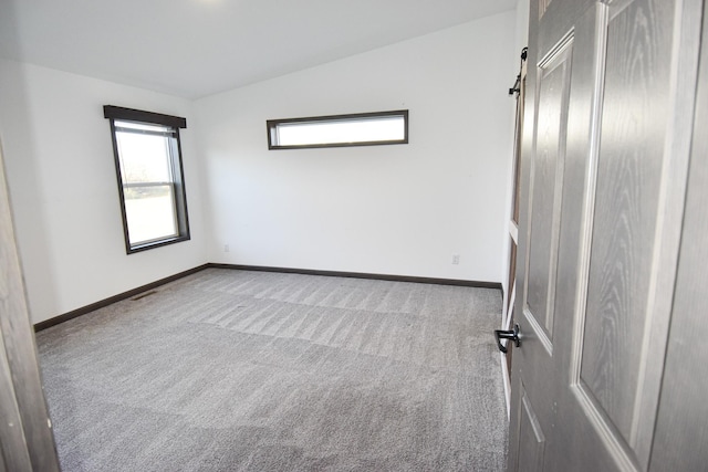 empty room with a barn door, vaulted ceiling, and carpet