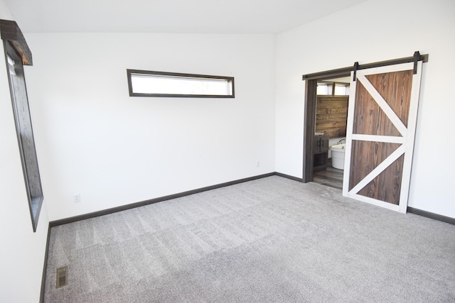 carpeted spare room with a barn door, a healthy amount of sunlight, and lofted ceiling