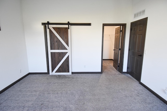 unfurnished bedroom featuring dark colored carpet, a spacious closet, a barn door, and a closet