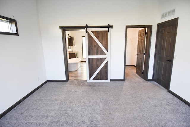 unfurnished bedroom featuring a barn door, a closet, a spacious closet, and carpet floors