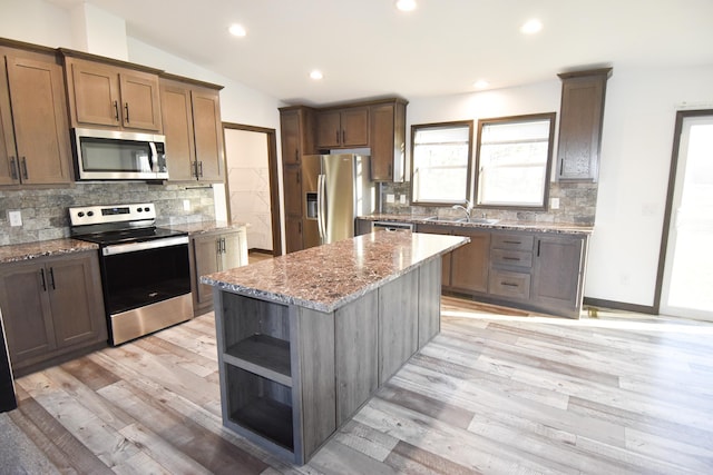 kitchen featuring stainless steel appliances, lofted ceiling, a kitchen island, and light hardwood / wood-style flooring