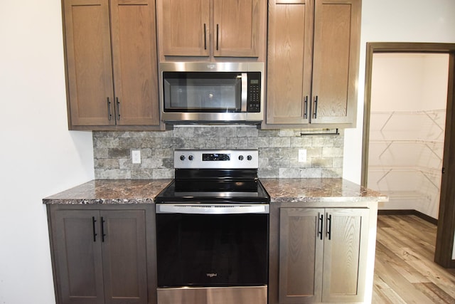 kitchen with dark stone countertops, light hardwood / wood-style flooring, appliances with stainless steel finishes, and tasteful backsplash