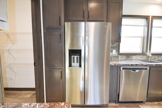 kitchen with sink, appliances with stainless steel finishes, dark stone countertops, dark brown cabinets, and decorative backsplash