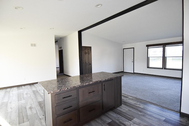 kitchen with hardwood / wood-style floors, vaulted ceiling, dark stone countertops, and a kitchen island