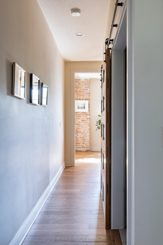 corridor featuring light hardwood / wood-style floors, a textured ceiling, and a barn door