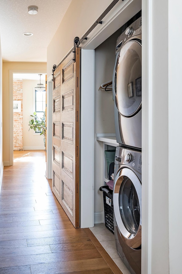 washroom with stacked washer / dryer, a barn door, and light hardwood / wood-style floors