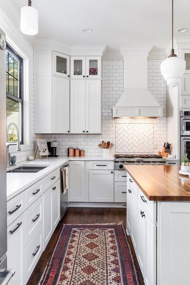 kitchen with crown molding, custom exhaust hood, white cabinetry, and decorative light fixtures