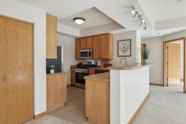 kitchen with track lighting, light colored carpet, appliances with stainless steel finishes, and kitchen peninsula