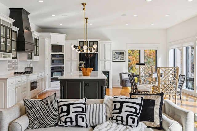 kitchen featuring a healthy amount of sunlight, a center island with sink, custom range hood, and hanging light fixtures