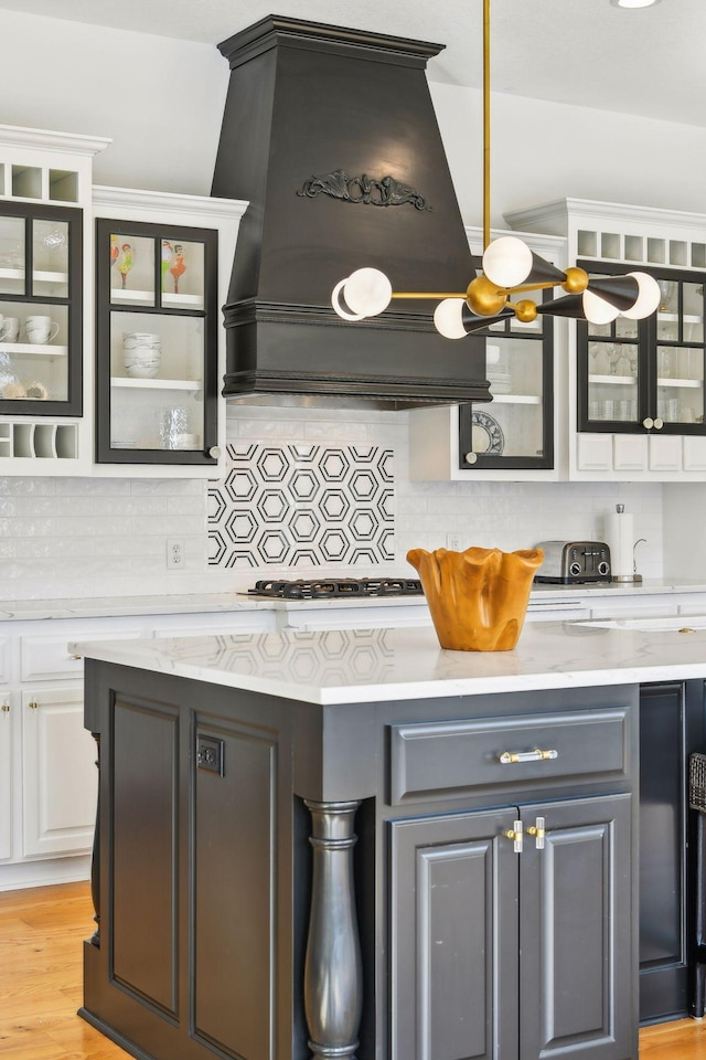 kitchen featuring decorative backsplash, premium range hood, white cabinetry, and light wood-type flooring