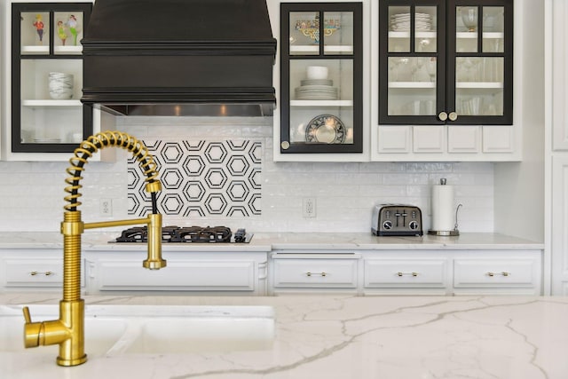 kitchen featuring stainless steel gas stovetop, decorative backsplash, light stone counters, and exhaust hood