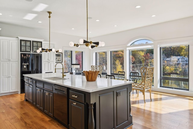 kitchen featuring light hardwood / wood-style flooring, a center island with sink, sink, light stone countertops, and black appliances