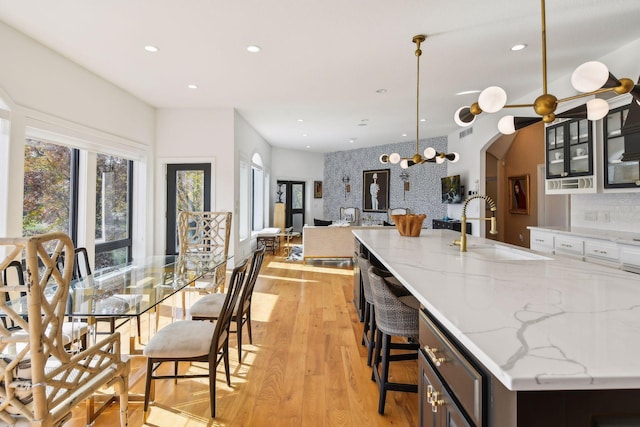 kitchen featuring sink, light wood-type flooring, a kitchen breakfast bar, decorative light fixtures, and light stone counters