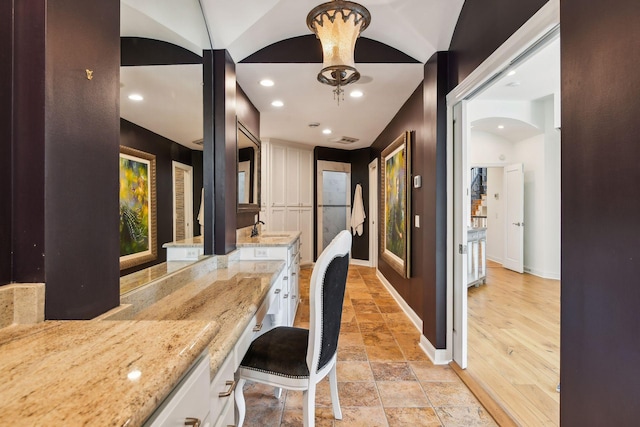 interior space with lofted ceiling, sink, white cabinets, light stone counters, and light hardwood / wood-style floors