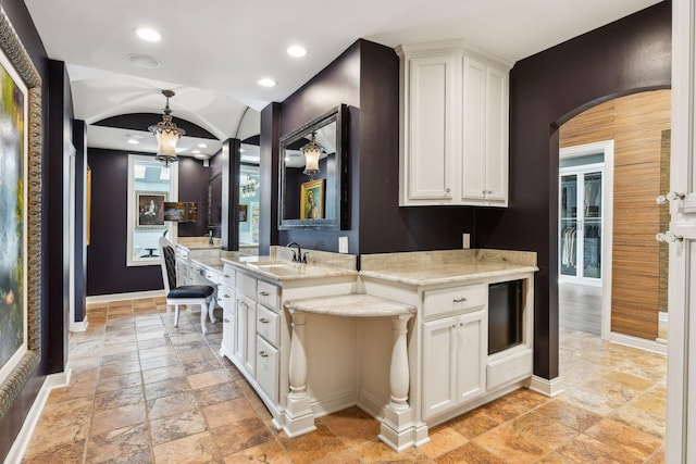 kitchen with white cabinetry, light stone countertops, sink, and pendant lighting