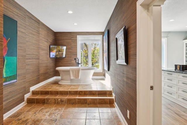 bathroom featuring vanity, wooden walls, a textured ceiling, and a washtub