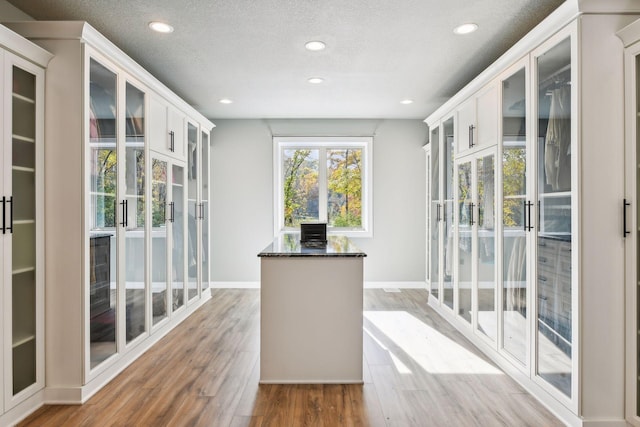 interior space with light hardwood / wood-style floors, white cabinets, a textured ceiling, and dark stone counters