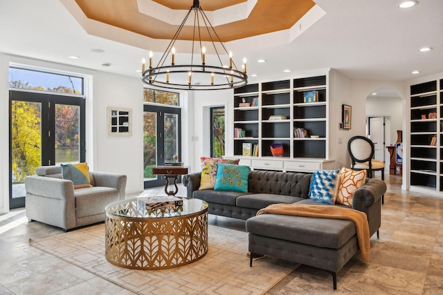 living room with built in features, a chandelier, plenty of natural light, and a raised ceiling