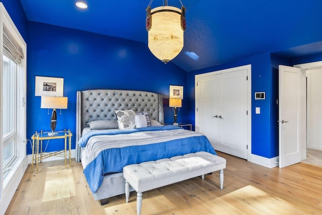 bedroom featuring a closet, multiple windows, wood-type flooring, and vaulted ceiling