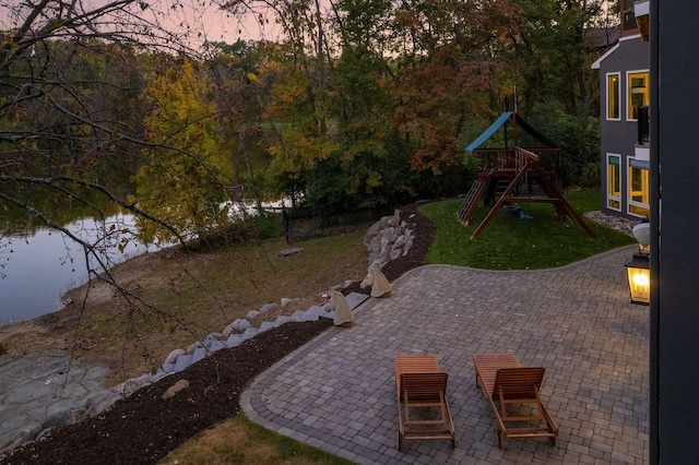 patio terrace at dusk featuring a playground, a yard, and a water view