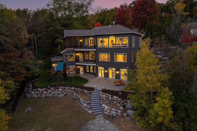 back house at dusk with a patio, a playground, and a balcony