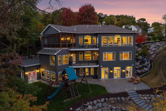 back house at dusk featuring a balcony and a playground