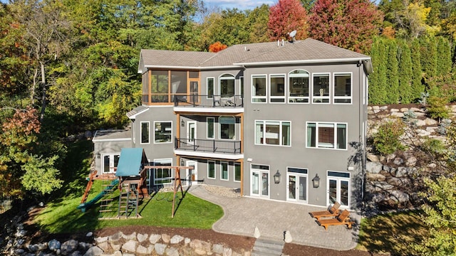 rear view of house featuring french doors, a playground, a lawn, and a balcony