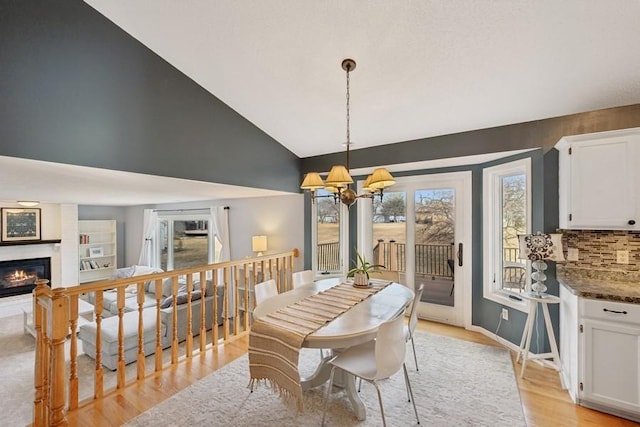 dining area with a chandelier, baseboards, vaulted ceiling, light wood-type flooring, and a glass covered fireplace