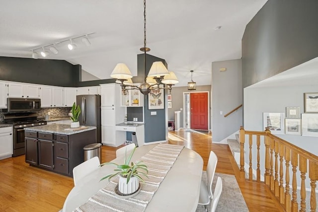 dining space with light wood-style floors, vaulted ceiling, track lighting, a chandelier, and stairs