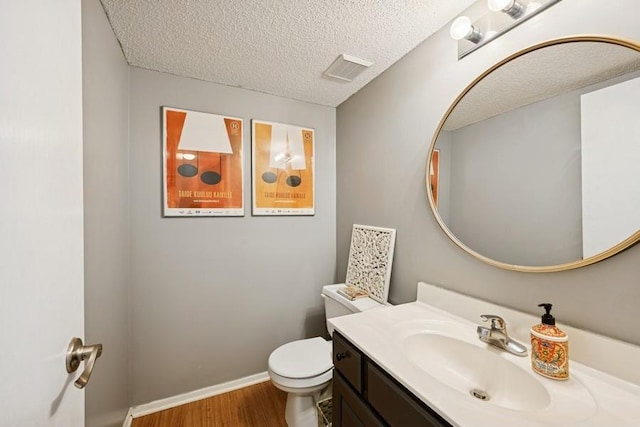 half bathroom with visible vents, toilet, wood finished floors, a textured ceiling, and vanity