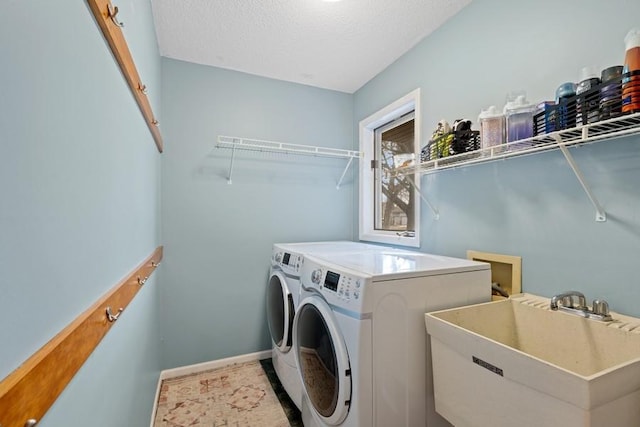 washroom with a sink, a textured ceiling, washer and dryer, laundry area, and baseboards