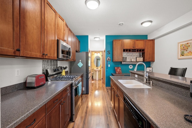 kitchen with light hardwood / wood-style floors, sink, backsplash, a textured ceiling, and appliances with stainless steel finishes