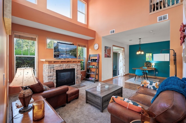 living room with a high ceiling, light hardwood / wood-style floors, a chandelier, and a stone fireplace