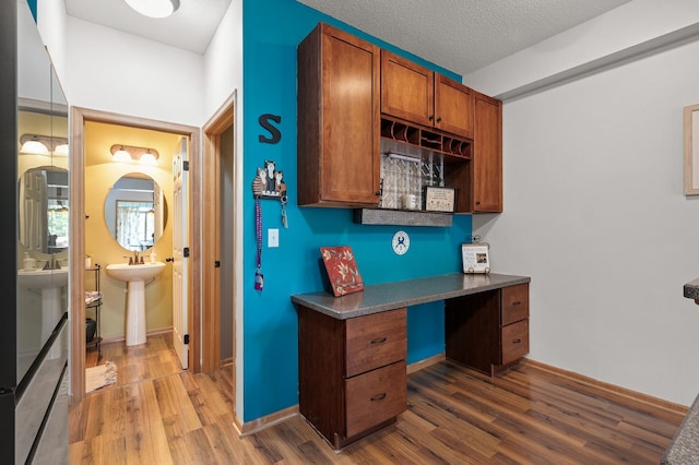 kitchen with wood finished floors, built in study area, a textured ceiling, dark countertops, and brown cabinets