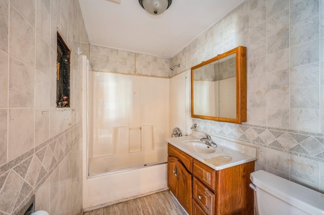 full bathroom featuring hardwood / wood-style floors, vanity, bath / shower combo with glass door, tile walls, and toilet