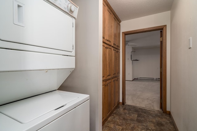 laundry area featuring cabinets, a baseboard heating unit, a textured ceiling, and stacked washer and clothes dryer