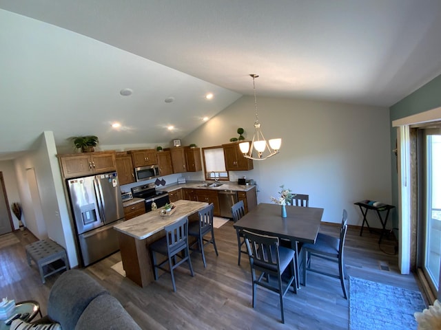 kitchen featuring stainless steel appliances, vaulted ceiling, wood-type flooring, and decorative light fixtures