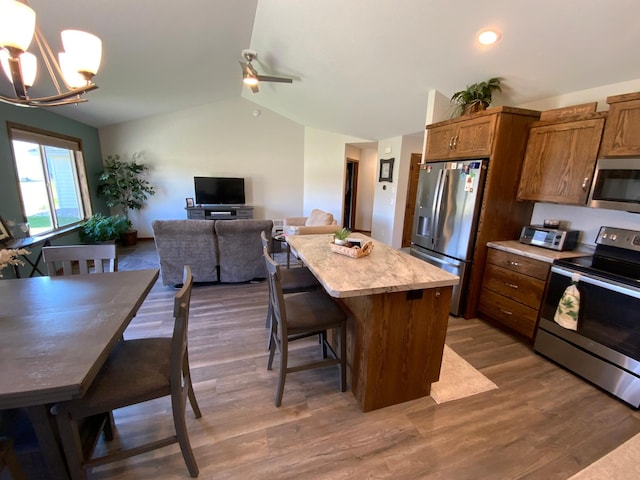 kitchen featuring a center island, dark hardwood / wood-style floors, lofted ceiling, appliances with stainless steel finishes, and decorative light fixtures