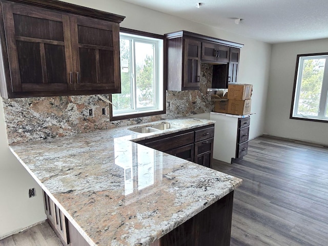 kitchen featuring hardwood / wood-style floors, light stone counters, kitchen peninsula, and backsplash