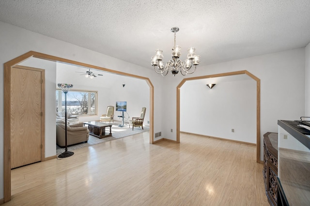 living room featuring ceiling fan with notable chandelier, a textured ceiling, and light wood-type flooring