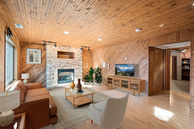 living room with rail lighting, wood ceiling, a large fireplace, wooden walls, and light hardwood / wood-style floors