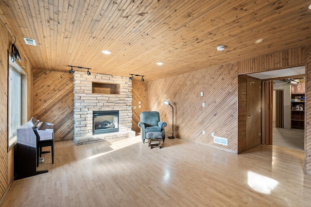 unfurnished living room with rail lighting, a stone fireplace, light hardwood / wood-style flooring, wooden ceiling, and wooden walls